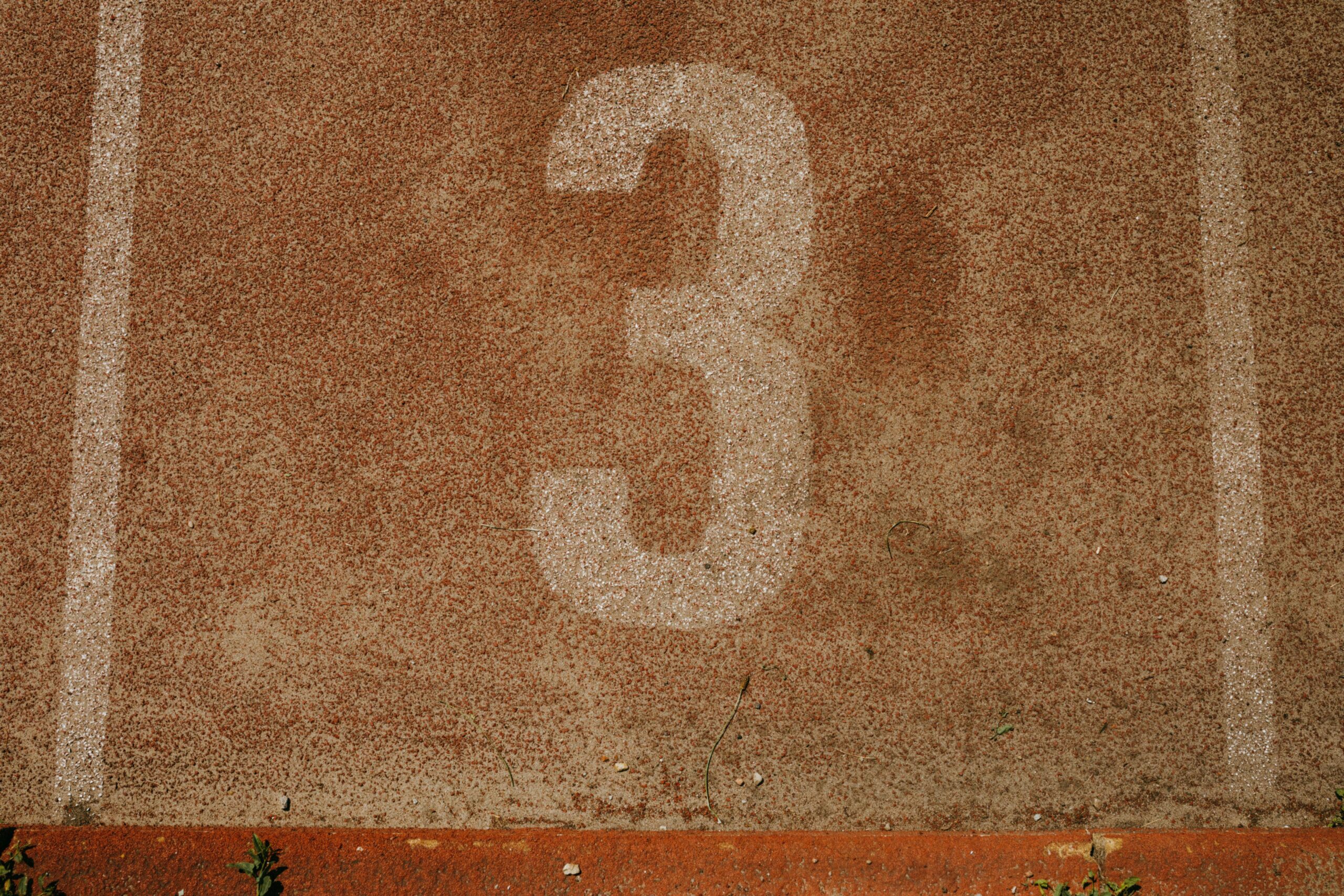 Close-up of a textured running track with the number three, showcasing sport simplicity and earthy tones.